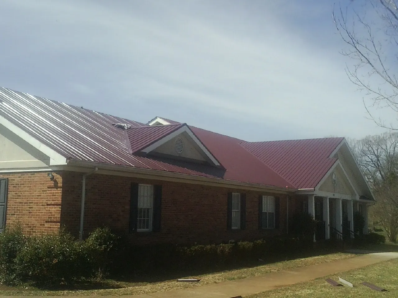 Red metal roof with gabled entries on a long brick building, from a Hail Damage Roof Repair job in Porterville
