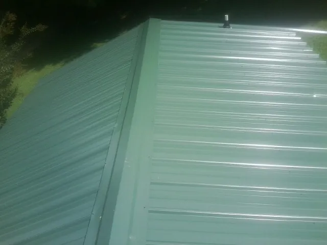 New green metal panels meeting at the ridge of a roof — Flat Roof Repair work by our crew in Porterville