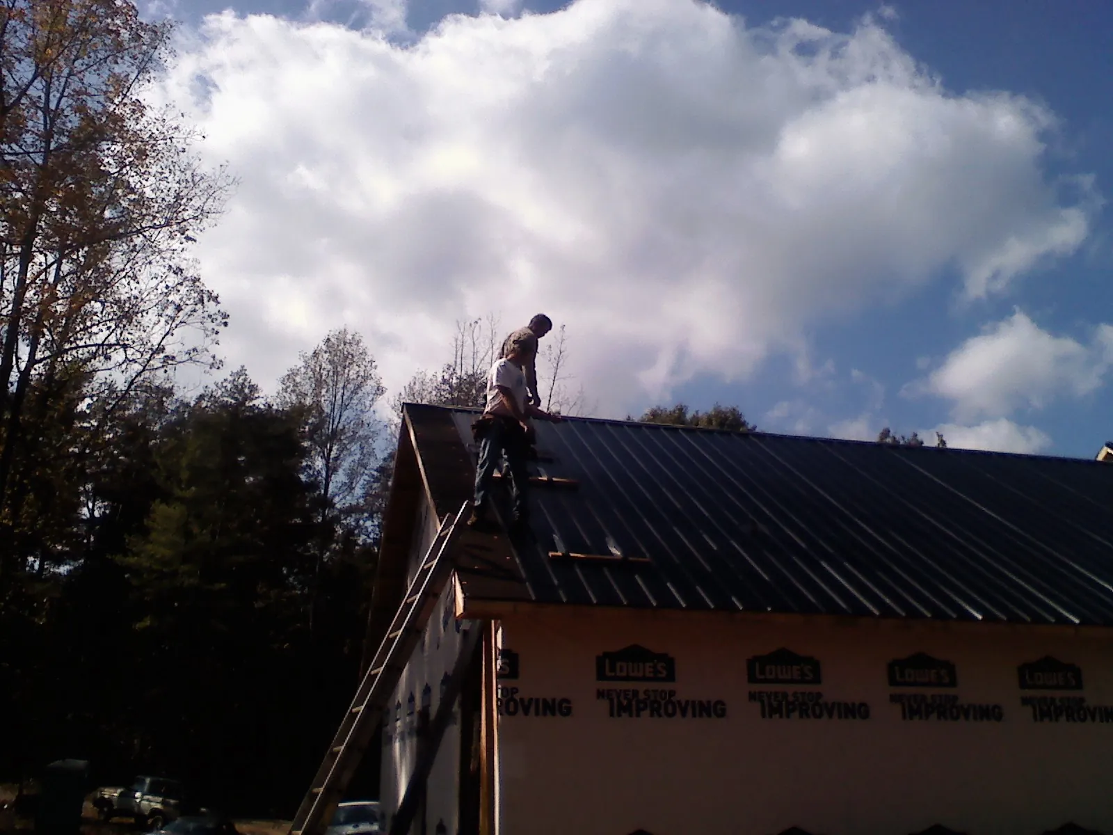 Roofer fastening dark metal panels high against a cloudy sky, from a Roof Inspection job in Porterville