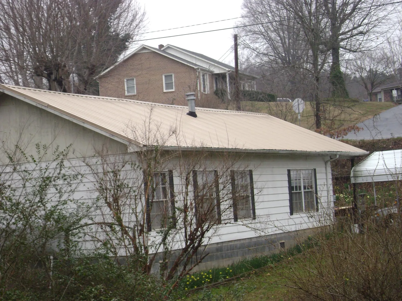 Tan metal roof on a white sided house set into a hillside — Commercial Roofing by Roofing Brothers in Porterville